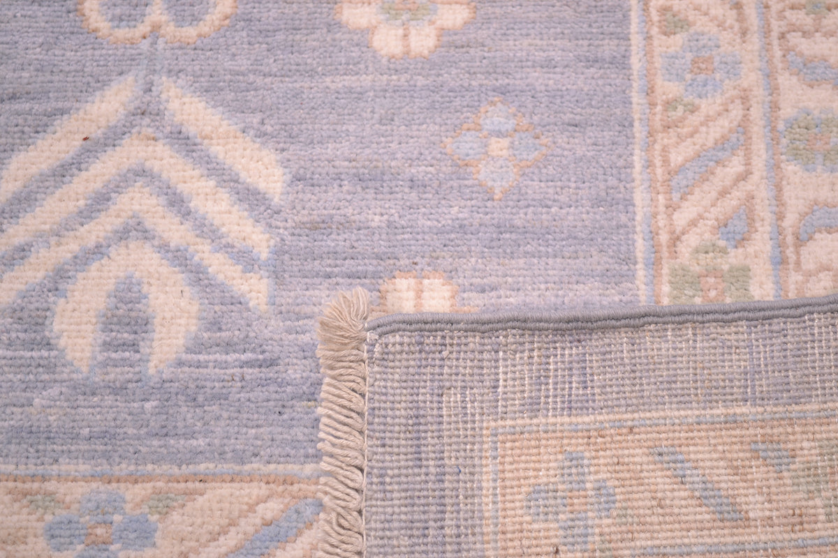 Rug edge close-up with beige fringe and pastel motif pattern on blue ground