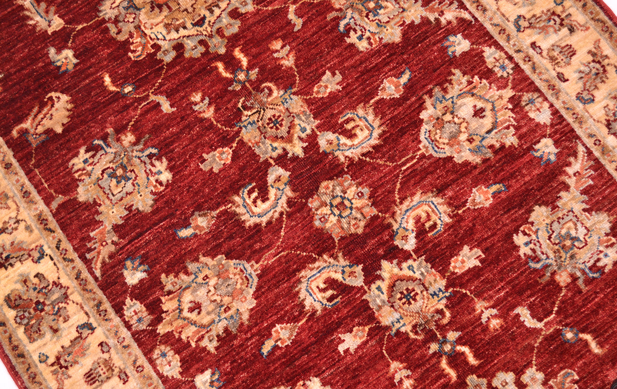 Detailed view of main field of handknotted rug with palmettes in blue, cream and terracotta on a red russet field.