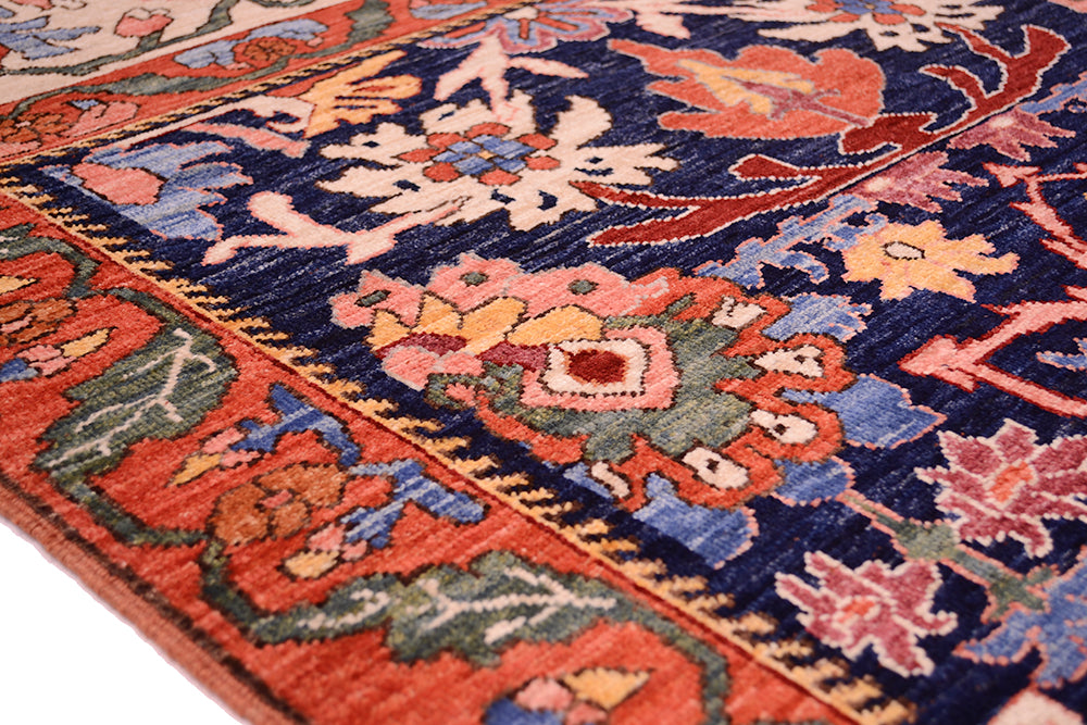Close-up corner of antique floral rug showing navy, orange, and green accents with border lines.