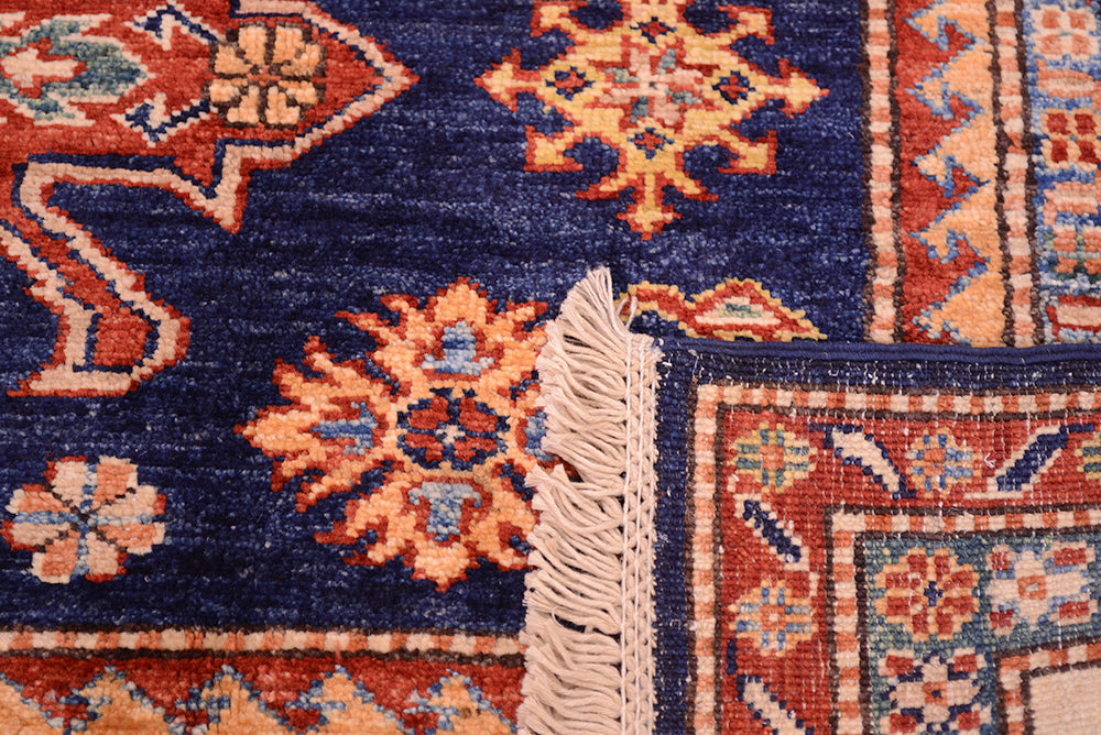 Close-up of the weave of a Navy blue handmade fine Kazak rug corner showing a deep navy blue field with cream, rust red, and light blue geometric medallions, plus a cream fringe edge.