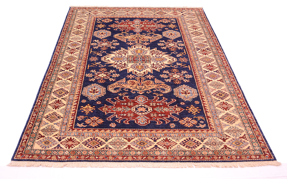 A traditional oriental fine Kazak area rug with a navy blue centre, beige and red borders, and cream fringe, shown flat against a white background.