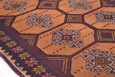 A close-up of a patterned old Afghan Belouch mat/small rug with a warm tan background, dark brown geometric hexagonal sections, and a dark border with multicoloured floral motifs.