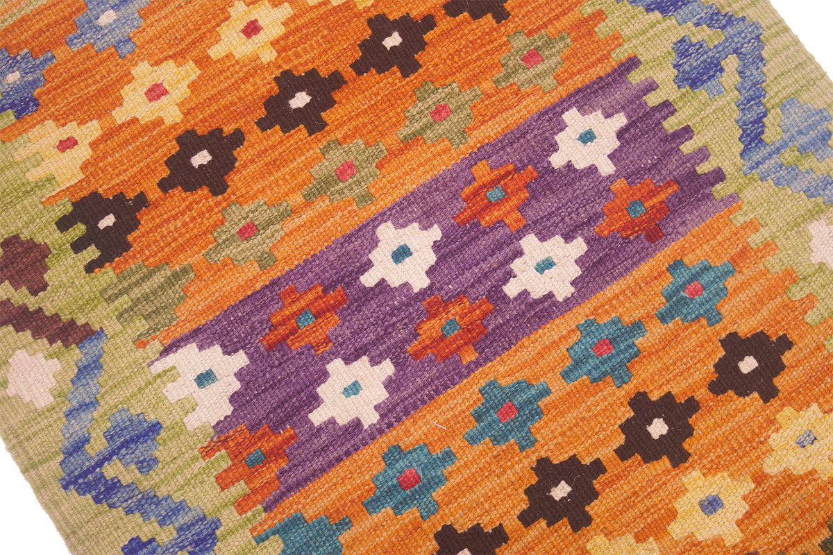A close-up of a handwoven Small Kilim featuring a vibrant geometric pattern with diagonal bands of orange, purple, blue, brown, and cream on a beige background.