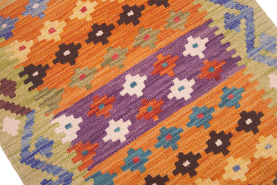 A close-up of a handwoven Small Kilim featuring a vibrant geometric pattern with diagonal bands of orange, purple, blue, brown, and cream on a beige background.