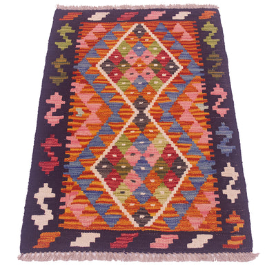 A flatweave kilim rug with a vibrant geometric pattern, featuring two large central diamond motifs and a dark purple border with fringe on the top and bottom edges.