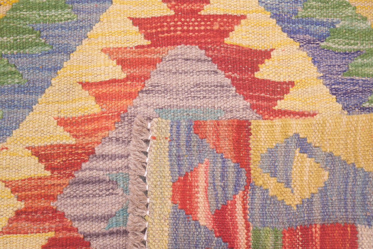 Close-up of a woven kilim rug with a geometric pattern in red, yellow, blue, green, and lavender, showing the textured wool pile and fringe edge.