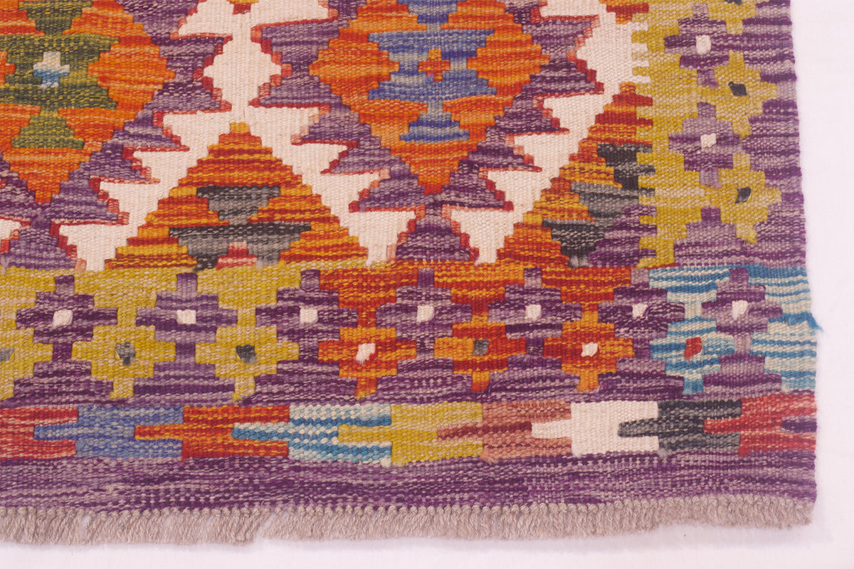 Kilim rug border detail in purple with colorful geometric bands and fringe.