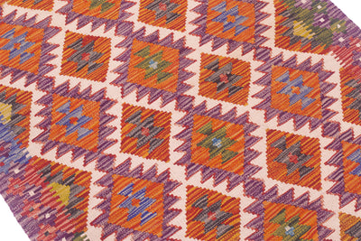 Kilim rug close-up: purple, orange, and white geometric squares and diamonds.