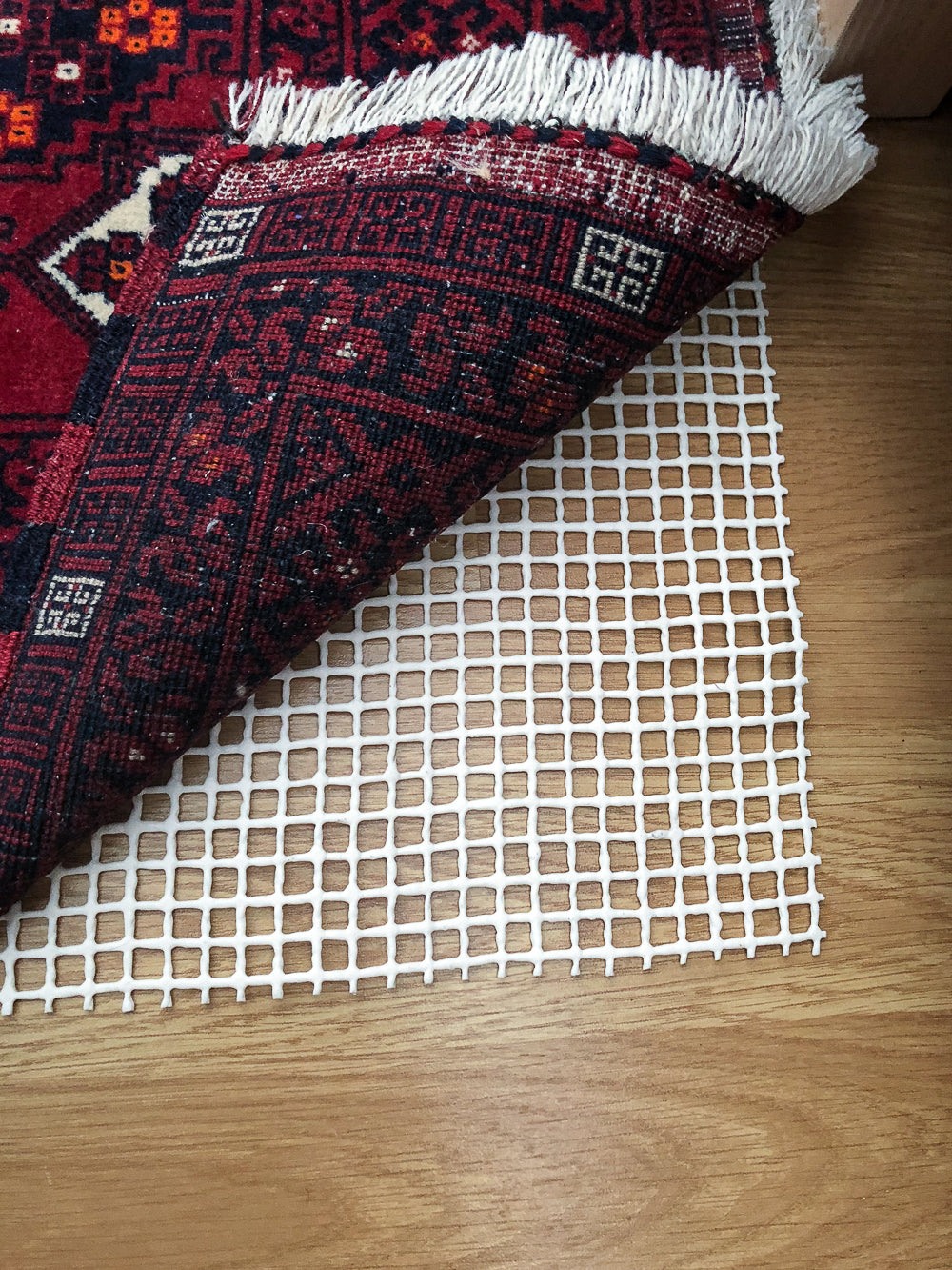 AKO Extra Anti-Slip Rug Underlay laid on a hard laminate wood floor with Red Afghan Rug on top.
