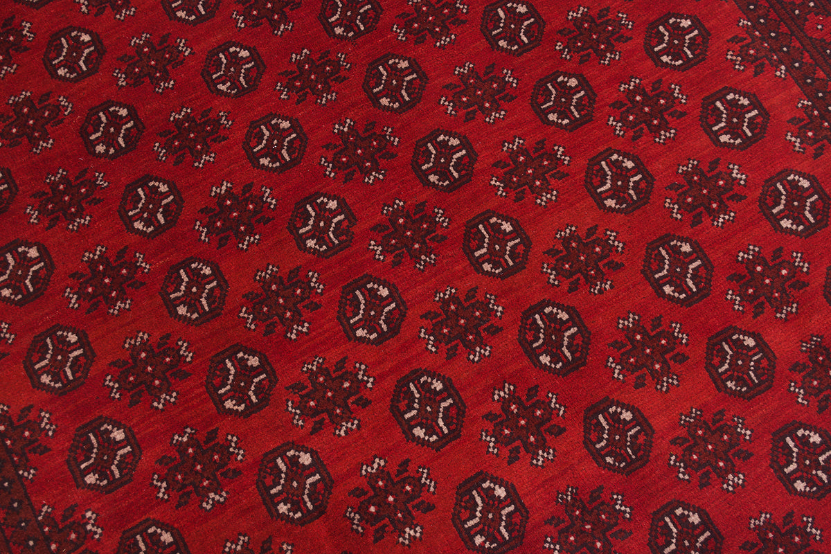 A close-up of a handmade red Afghan carpet pattern featuring repeating dark brown and beige geometric medallion motifs.