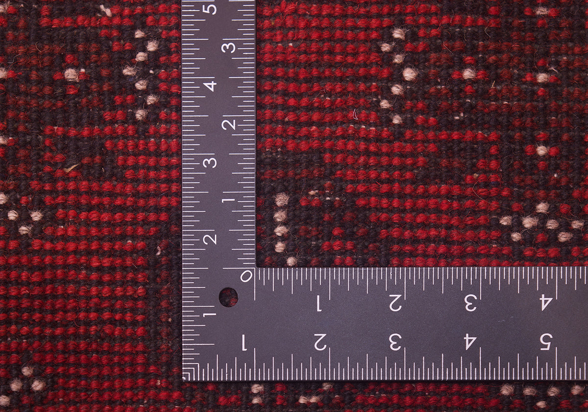 Close-up of a red and black Afghan handmade carpet with small light beige dots, shown with a metal L-square ruler to show scale of the hand-knotted weave.