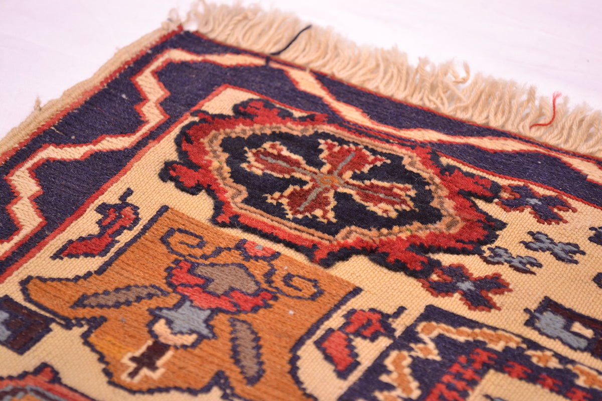 A close-up of a traditional patterned Afghan Soumak rug showing its cream base, navy blue borders, and red and orange central medallions with fringed edges.