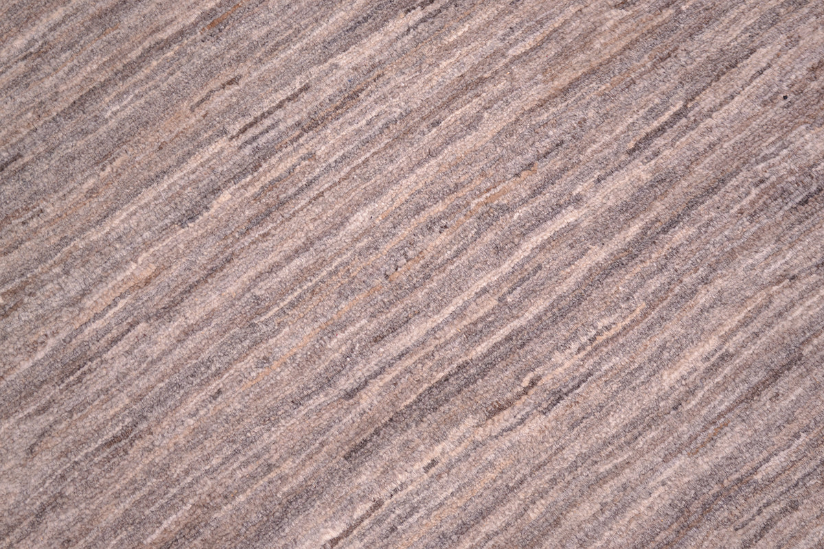 A close-up texture shot of a woven gabbeh plain rug with a subtle striped pattern in shades of taupe, brown, and beige.