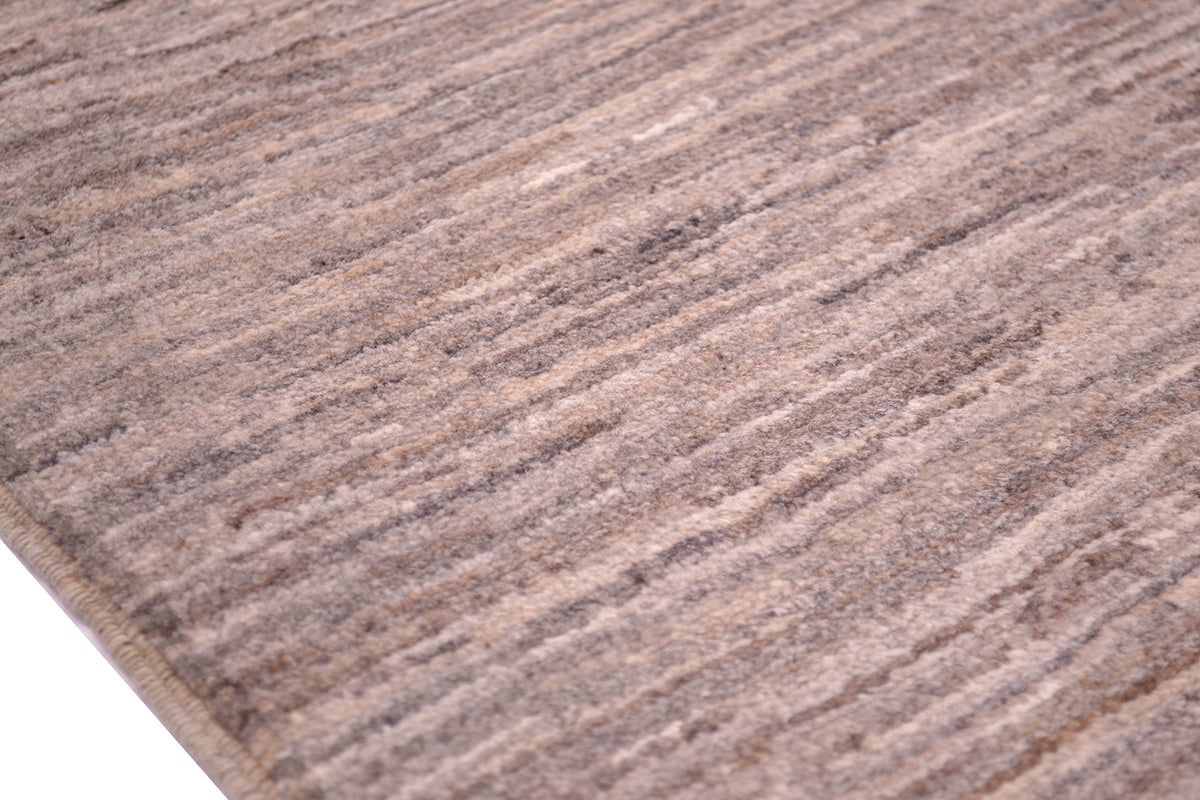 A close-up of a textured gabbeh area rug with a subtle striped pattern in shades of taupe, brown, and beige.