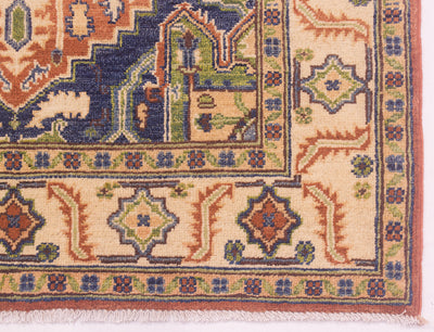 Close-up of a patterned Afghan Heriz rug corner showing cream, rust, navy, green, and blue geometric and floral motifs with a fringed edge.