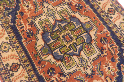 A close-up of a traditional patterned Heriz rug with a central medallion in cream, rust orange, blue, green, and beige.
