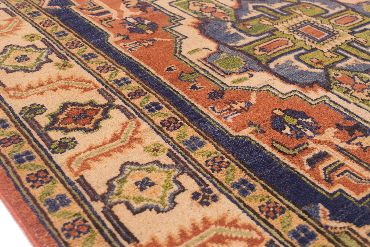 A close-up of a traditional patterned Heriz handmade rug with geometric and floral motifs in beige, rust orange, navy blue, olive green, and brown.