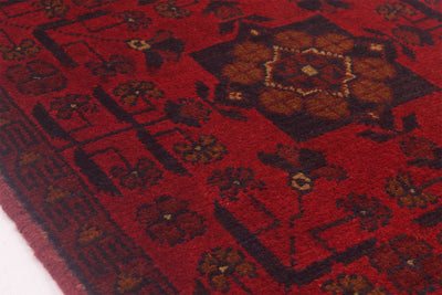 A close-up of a red patterned Afghan runner rug with dark brown and beige geometric and floral motifs.