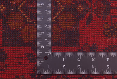 Close-up of back of a patterned runner rug with L-shaped ruler placed over it to show scale, featuring a red, brown, and black woven design.