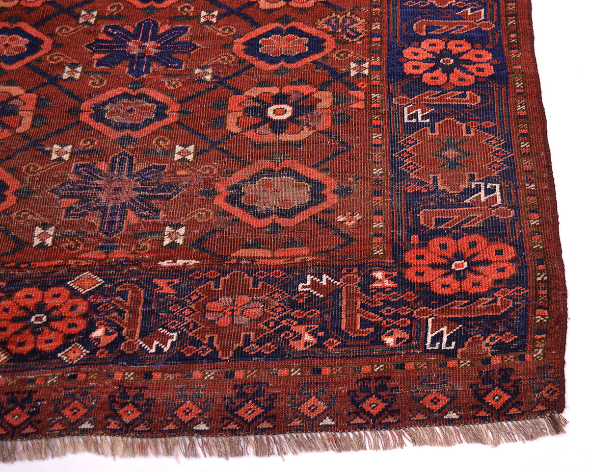 A close-up of a patterned Antique Ersari Chuval corner showing a dark red field with navy blue, rust orange, and beige geometric and floral motifs, finished with fringed edges.