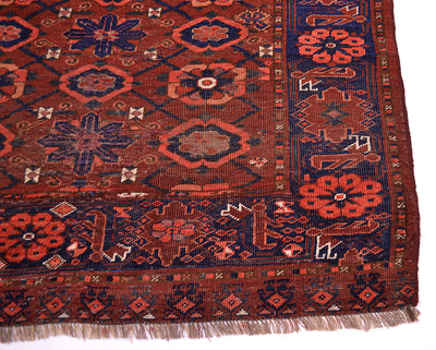 A close-up of a patterned Antique Ersari Chuval corner showing a dark red field with navy blue, rust orange, and beige geometric and floral motifs, finished with fringed edges.