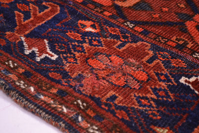 A close-up of an Antique Ersari Chuval rug showing a detailed repaired woven design in rust red, navy blue, and cream.