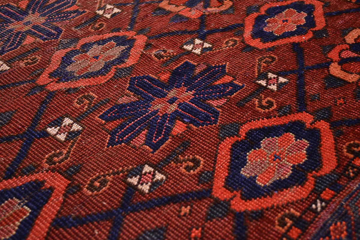 Close-up of a hand-knotted antique Ersari Chuval/Juval rug or textile with a geometric floral pattern in rust red, navy blue, and orange.