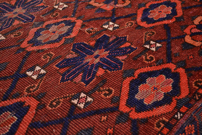 Close-up of a hand-knotted antique Ersari Chuval/Juval rug or textile with a geometric floral pattern in rust red, navy blue, and orange.