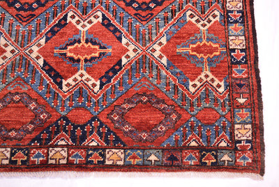A close-up of a corner of a traditional fine antique style Beshir rug showing rust-red, blue, and beige geometric motifs and borders.
