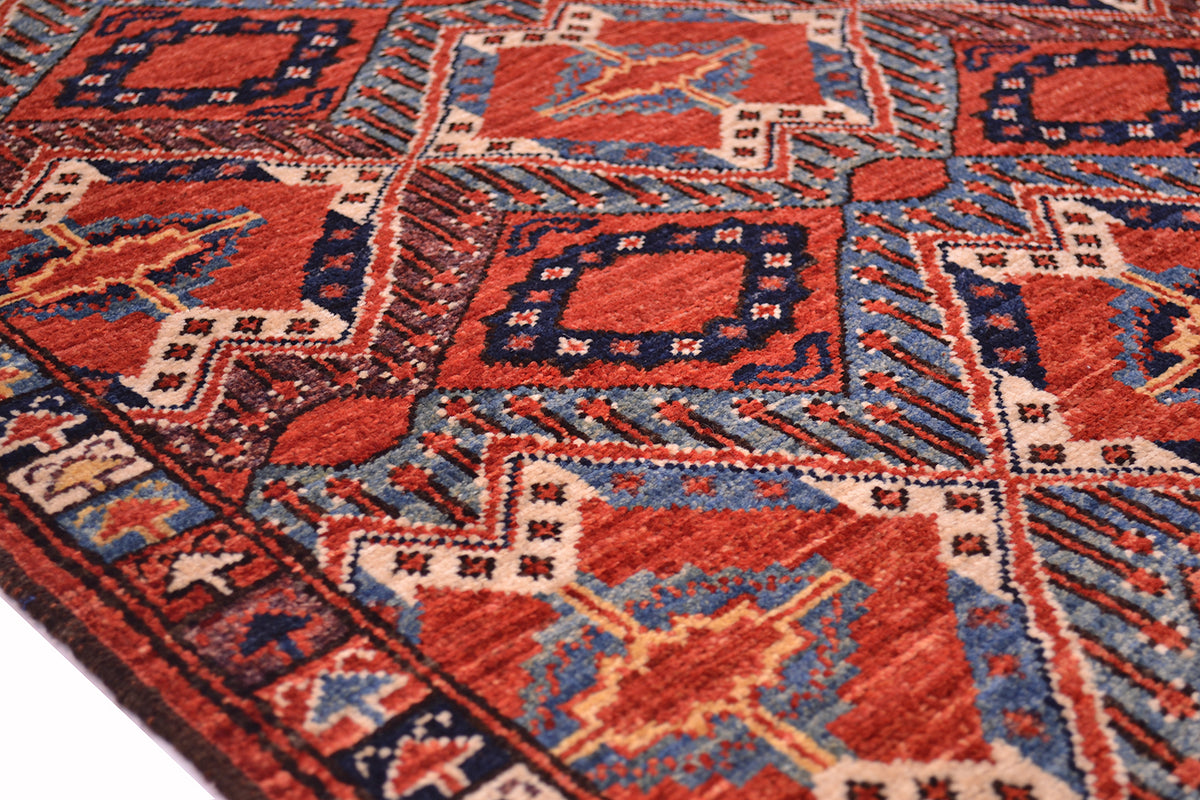 A close-up of a traditional patterned antique finish Turkmen Beshir rug with geometric and floral motifs in rust-red, blue, beige, and brown.