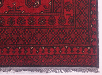 A close-up of a red and black Afghan Oriental Bokhara rug corner with grey fringe visible along the bottom edge.