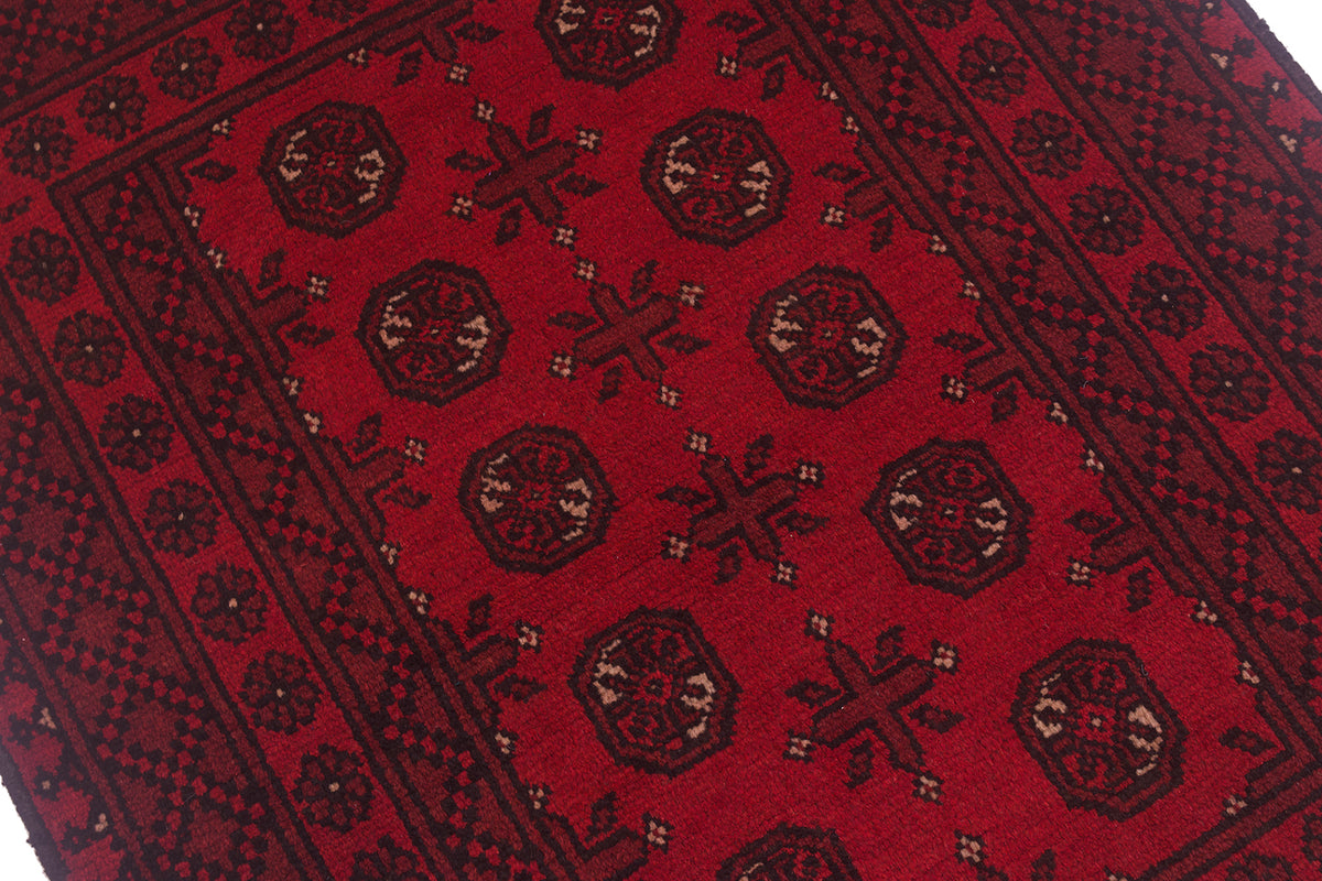 A close-up of a red patterned Afghan Bokhara rug with dark brown and beige geometric motifs and borders.