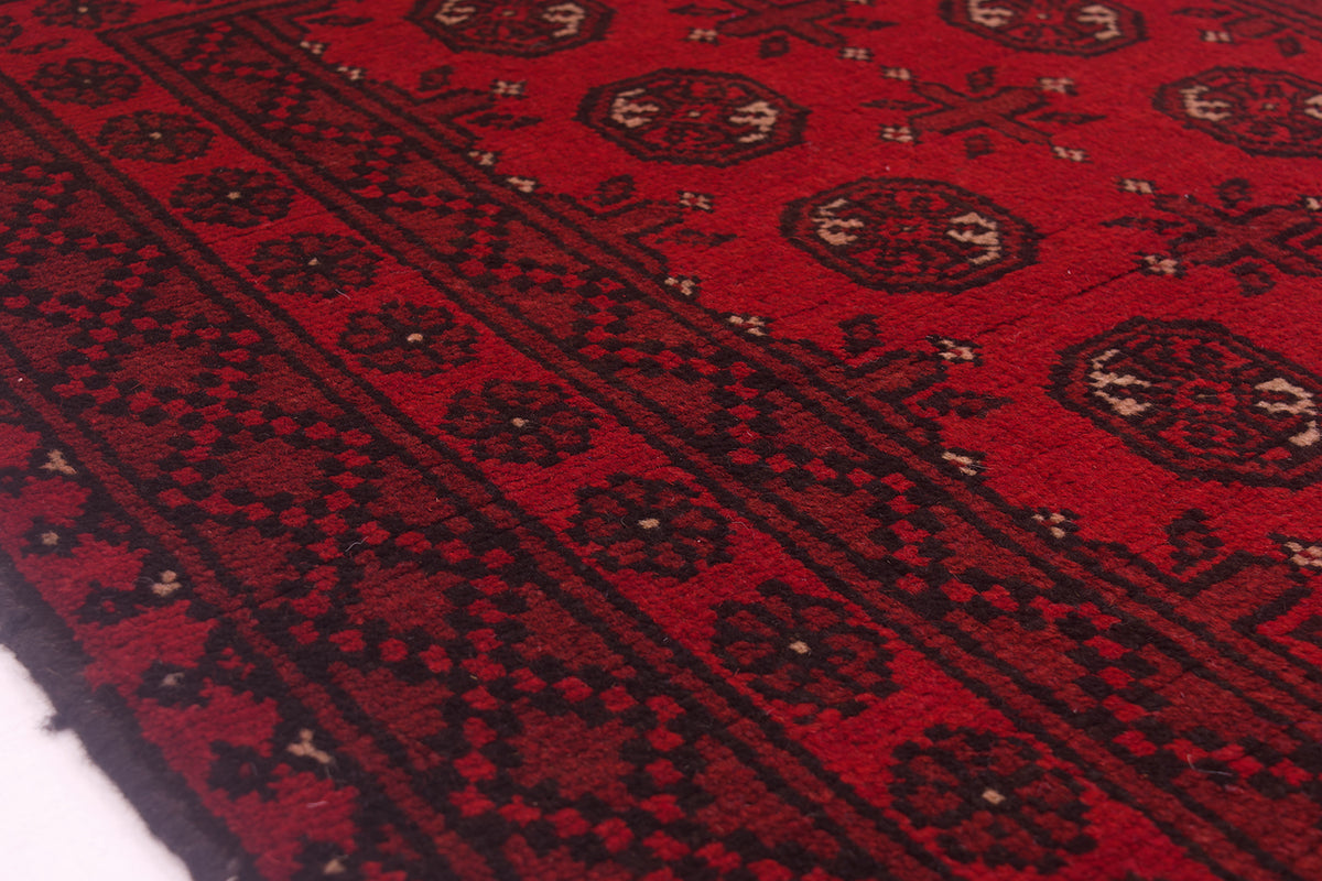 A close-up of a red patterned Afghan Aqcha rug with black geometric borders and motifs, showing the detailed woven texture.