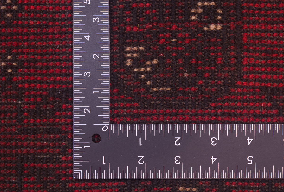 Close-up of a hand-knotted back of a red Afghan rug with a metal L-square ruler placed over the corner to show scale of the knotted weave. 