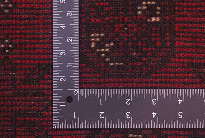Close-up of a hand-knotted back of a red Afghan rug with a metal L-square ruler placed over the corner to show scale of the knotted weave. 