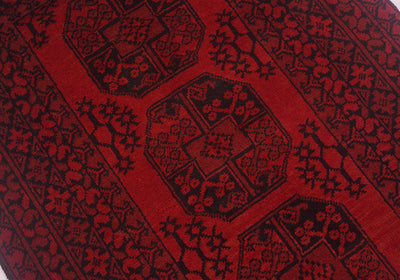 A close-up of a red and black patterned Fil Pai Afghan rug with geometric and floral motifs.