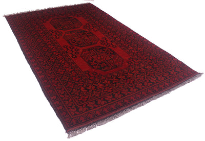 A rectangular red and black Afghan rug with fringed edges, shown at an angle on a plain white background.