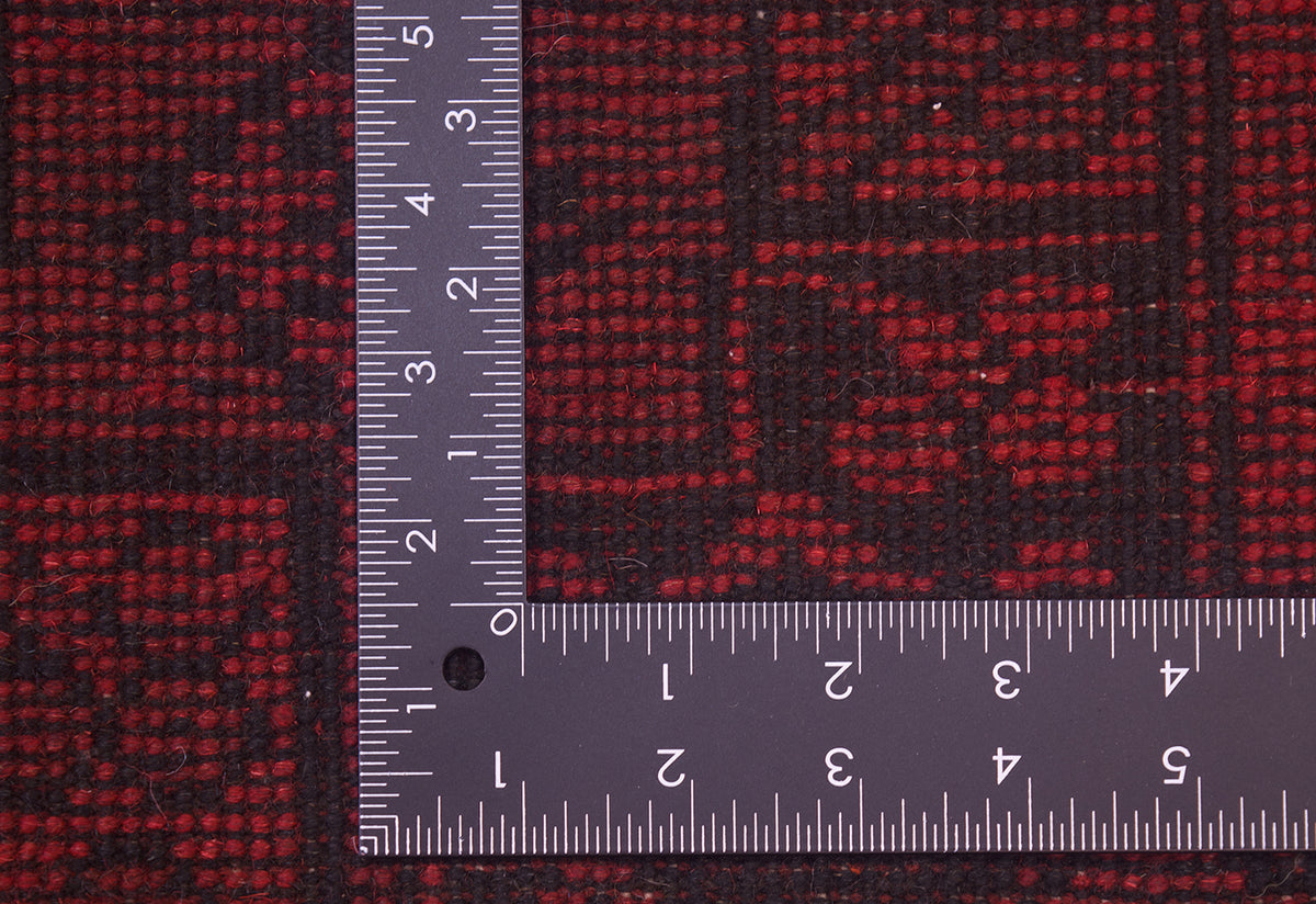A close-up of the hand-knotted back of a a dark red and black Afghan rug with a metal L-square ruler placed at the corner to show the scale of the knotted back.