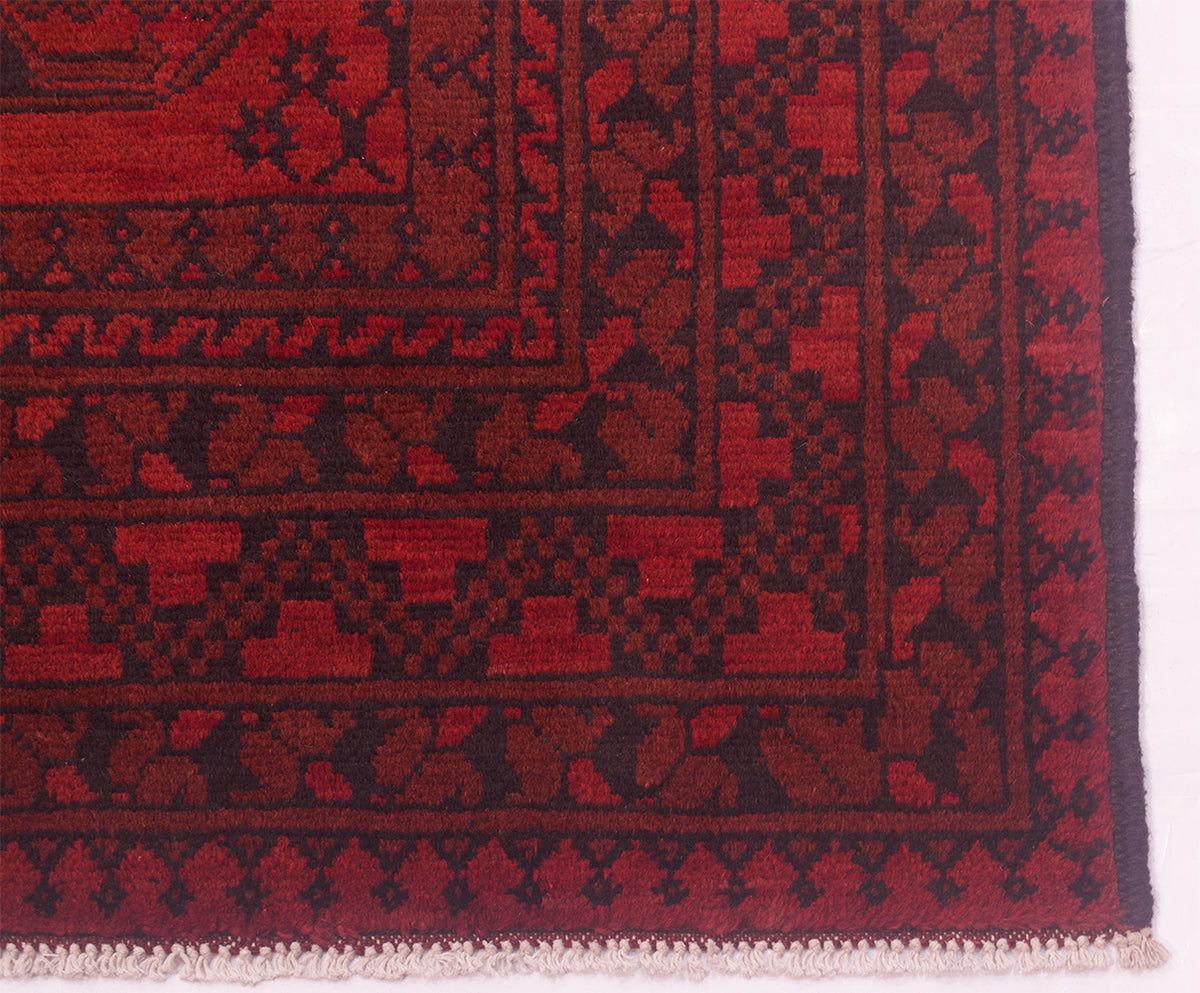 Close-up of a patterned Afghan Aqcha rug corner showing deep red and black woven geometric borders with white fringe at the bottom.