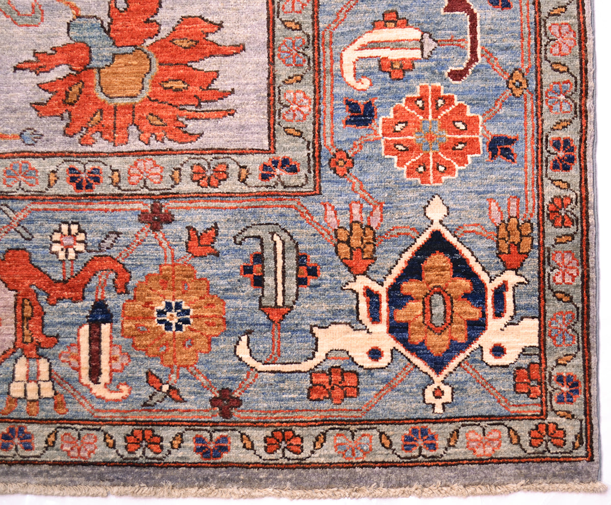 Detail of border and corner of large Afghan Carpet inspired by antique Persian carpet design. Blue border with angular boteh and rosettes with traditional cloudband border pattern. Orange, amber, cream and dark blue accents.