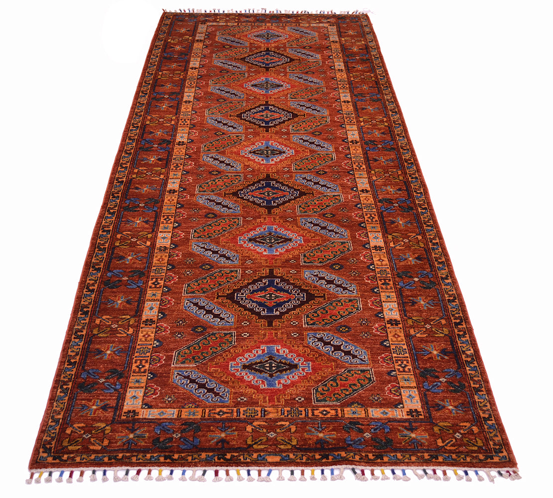 A traditional tribal runner with a warm cinnamon background, featuring a central field of blue and beige geometric medallions and a detailed border, shown flat against a white background.