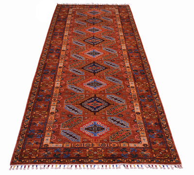 A traditional tribal runner with a warm cinnamon background, featuring a central field of blue and beige geometric medallions and a detailed border, shown flat against a white background.