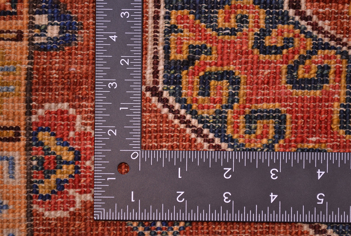 Close-up of back of a traditional rug with a dark ruler placed over it to show scale, showing a cinnamon, navy, and beige woven design.