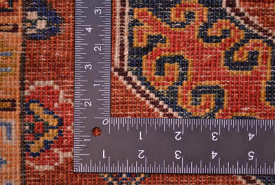 Close-up of back of a traditional rug with a dark ruler placed over it to show scale, showing a cinnamon, navy, and beige woven design.
