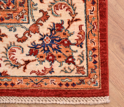 Close-up corner view of a traditional patterned Afghan Bakhtiar rug with an off-white main border, rust red edge, and blue floral accents, shown on a light wood floor.