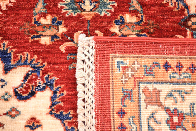 Close-up of a corner turned up of a patterned handmade Bakhtiar carpet showing a red field, cream and coral border, blue floral details, and a white woven fringe edge.