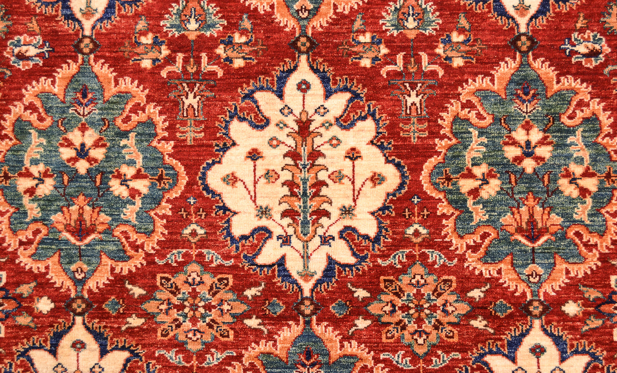 A close-up of a traditional patterned Afghan Persian designed rug with a red field, cream central medallion, and blue and peach floral motifs.