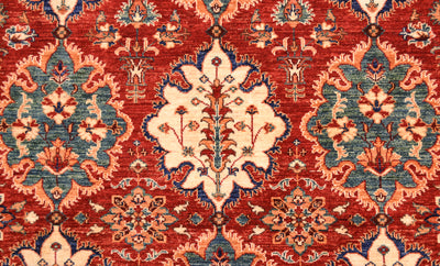 A close-up of a traditional patterned Afghan Persian designed rug with a red field, cream central medallion, and blue and peach floral motifs.