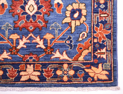 A close-up of a patterned handmade Afghan Aryana rug showing a blue field with floral motifs in rust red, beige, and navy, finished with a fringed edge.