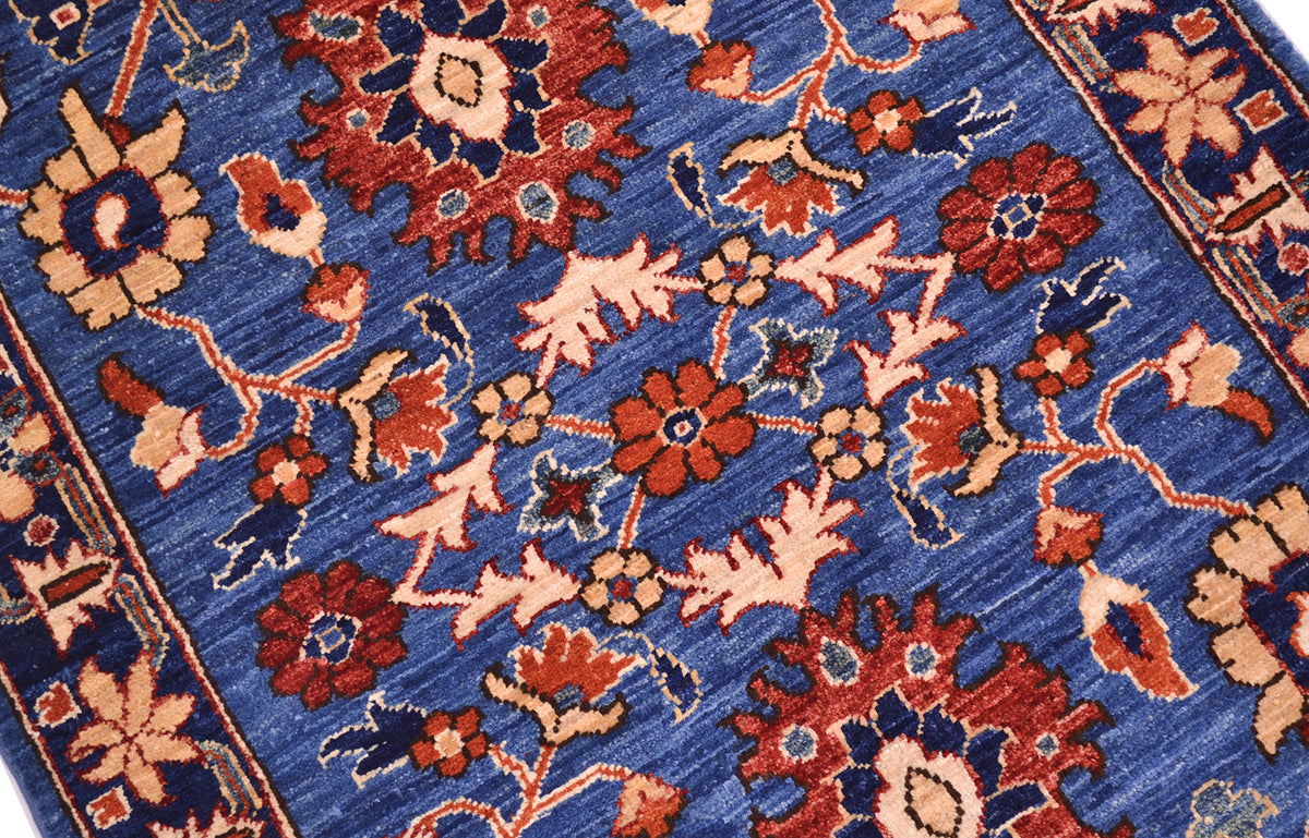 A close-up of a traditional patterned Aryana Afghan rug with a medium blue field, featuring red, orange, and beige floral motifs and a matching border.